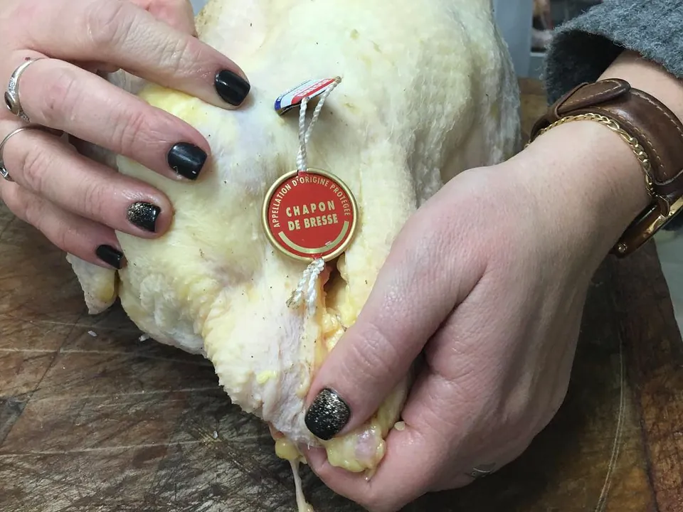 A Bresse capon held in two hands, its appellation ring visible at the leg.