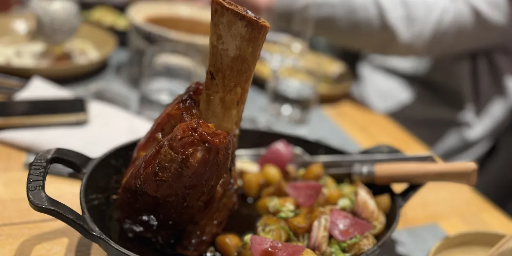 A glazed shank standing on its bone in a cast-iron dish, surrounded by potatoes.