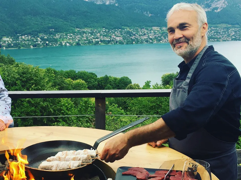 Hervé, chef at Les Terrasses du Lac, searing cuts of meat on his plancha, lake Annecy behind him.