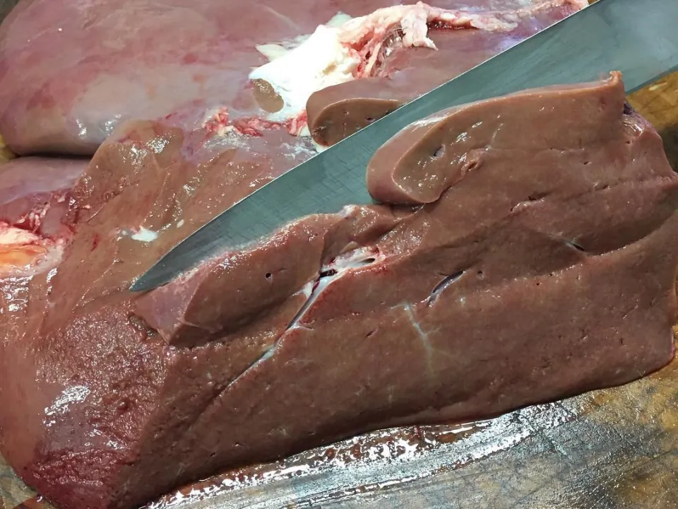 A calf’s liver being sliced with a knife on the block.