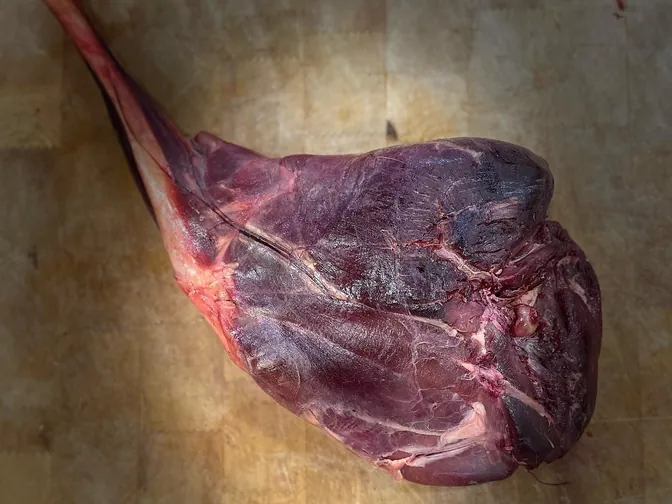 A dark-fleshed haunch of game on a butcher’s block.