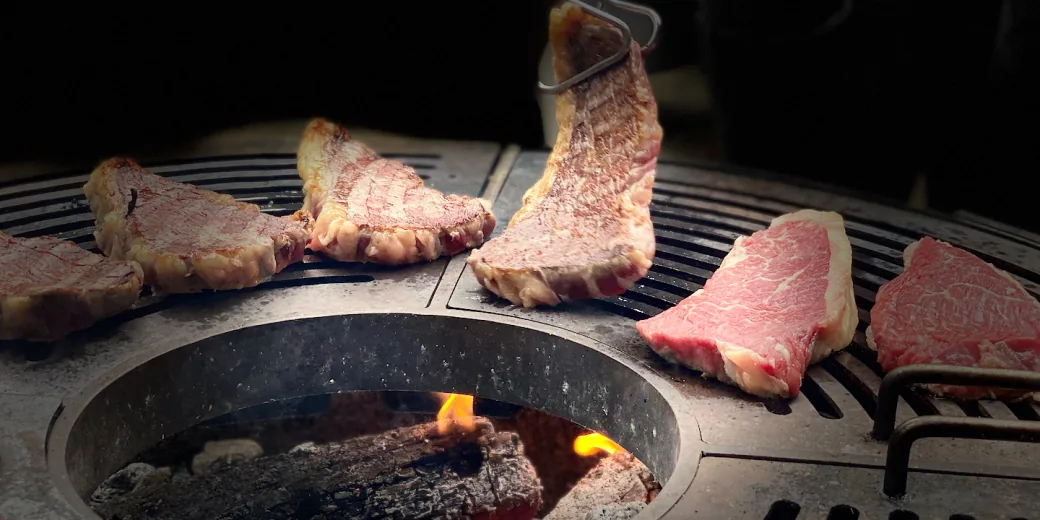 Cuts of beef on the plancha, embers glowing at the centre, and marbled raw pieces waiting