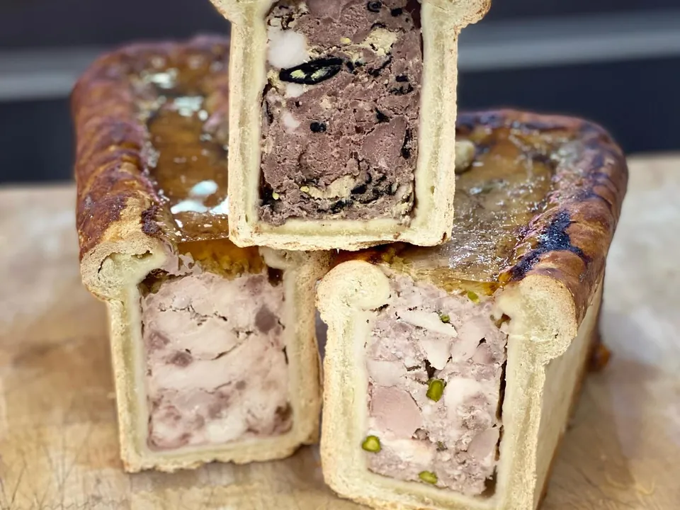 Several pâtés en croûte cut open, their fillings showing, pistachios and foie gras.