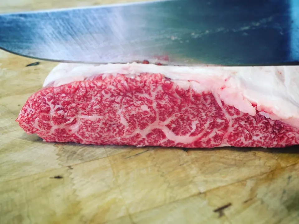 A slice of beef with very dense marbling, under the knife.