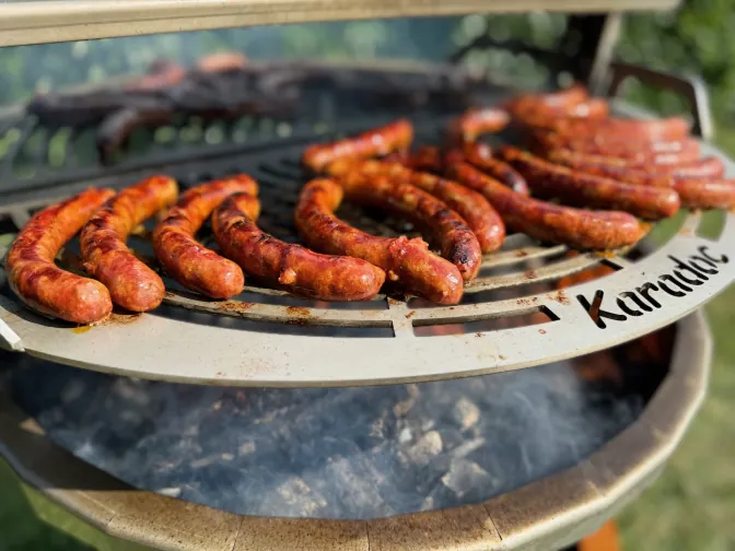 Des saucisses dorées sur la plaque d’un brasero, la fumée monte.
